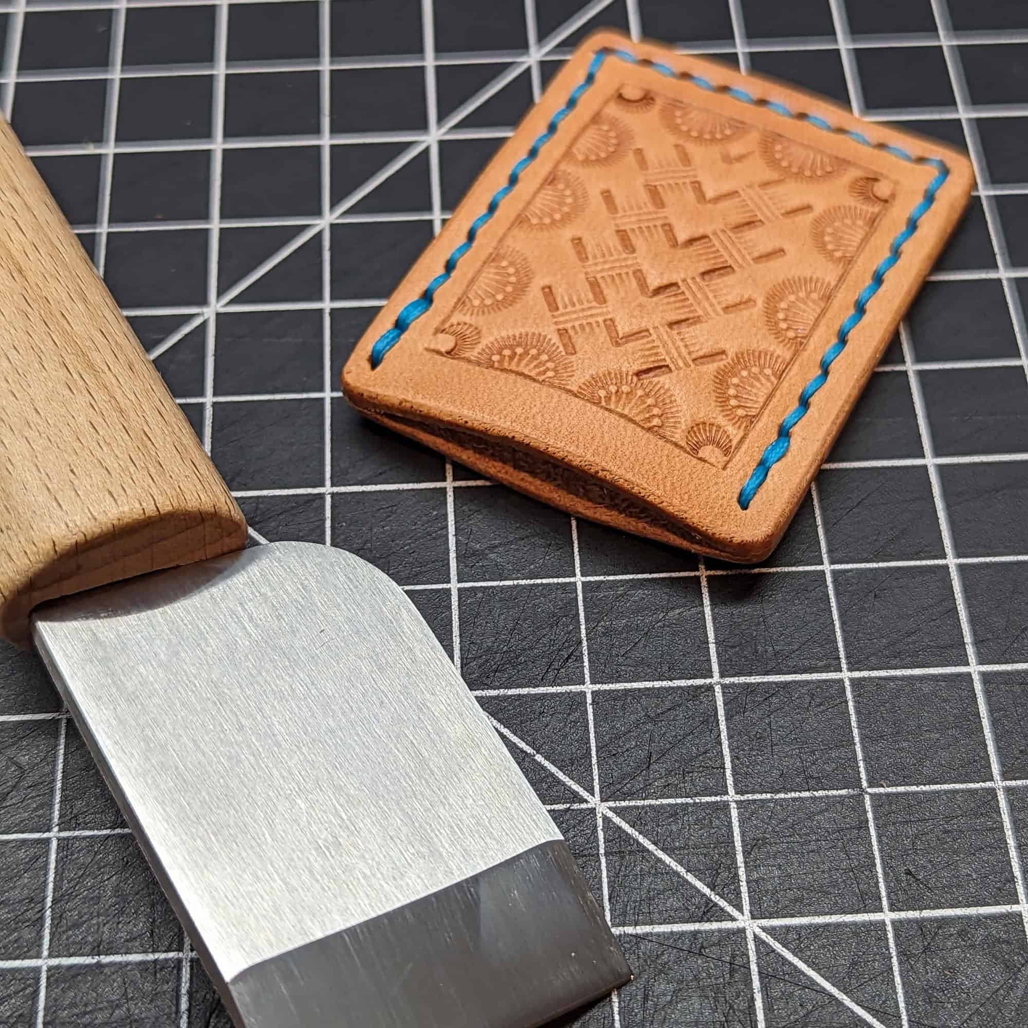 A skiving knife with a leather cover stamped in a basketweave pattern.