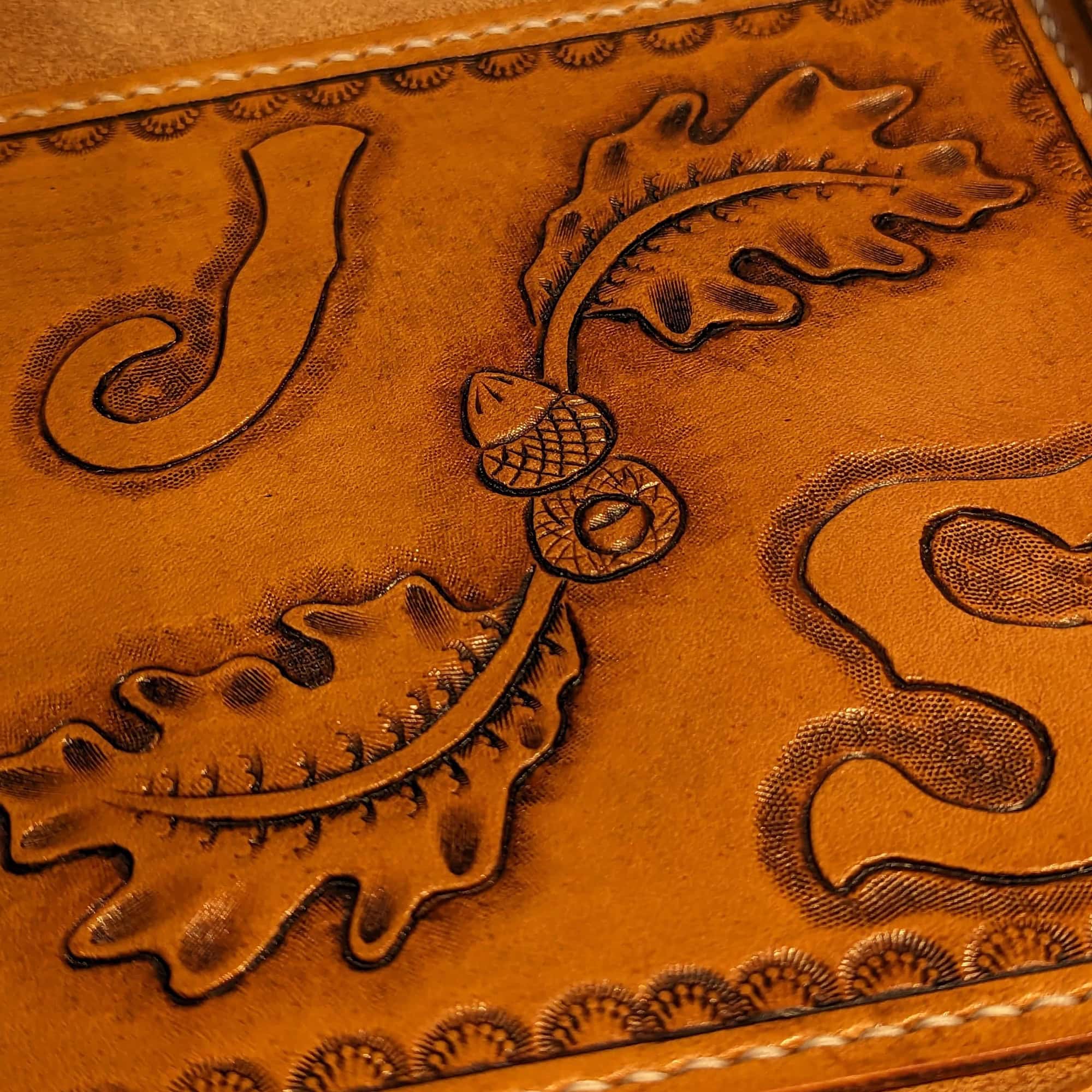 Leather valet tray tooled with the letters J and S with images of oak leaves and acorns.