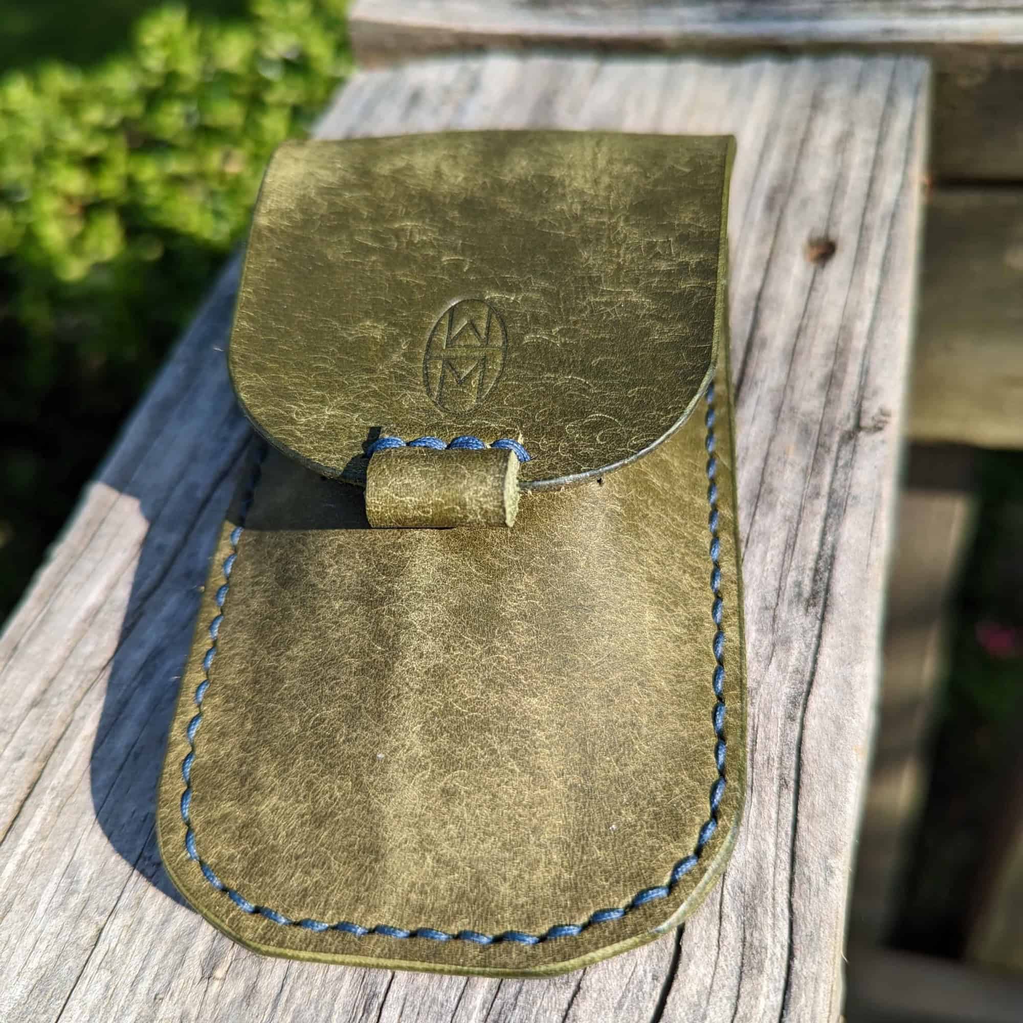 Leather watch case sitting on a wood rail.